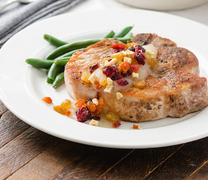 fruitons® All American Dried Fruit Blend as a premium ingredient adding color, texture, and fiber to meals, displayed on a grilled pork chop with sautéed fruit topping.